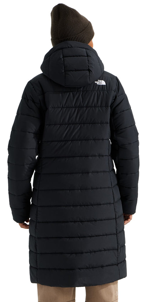 A back view of a person wearing a black, knee-length, hooded quilted puffer coat and a brown beanie hat, with a small white logo near the right shoulder.