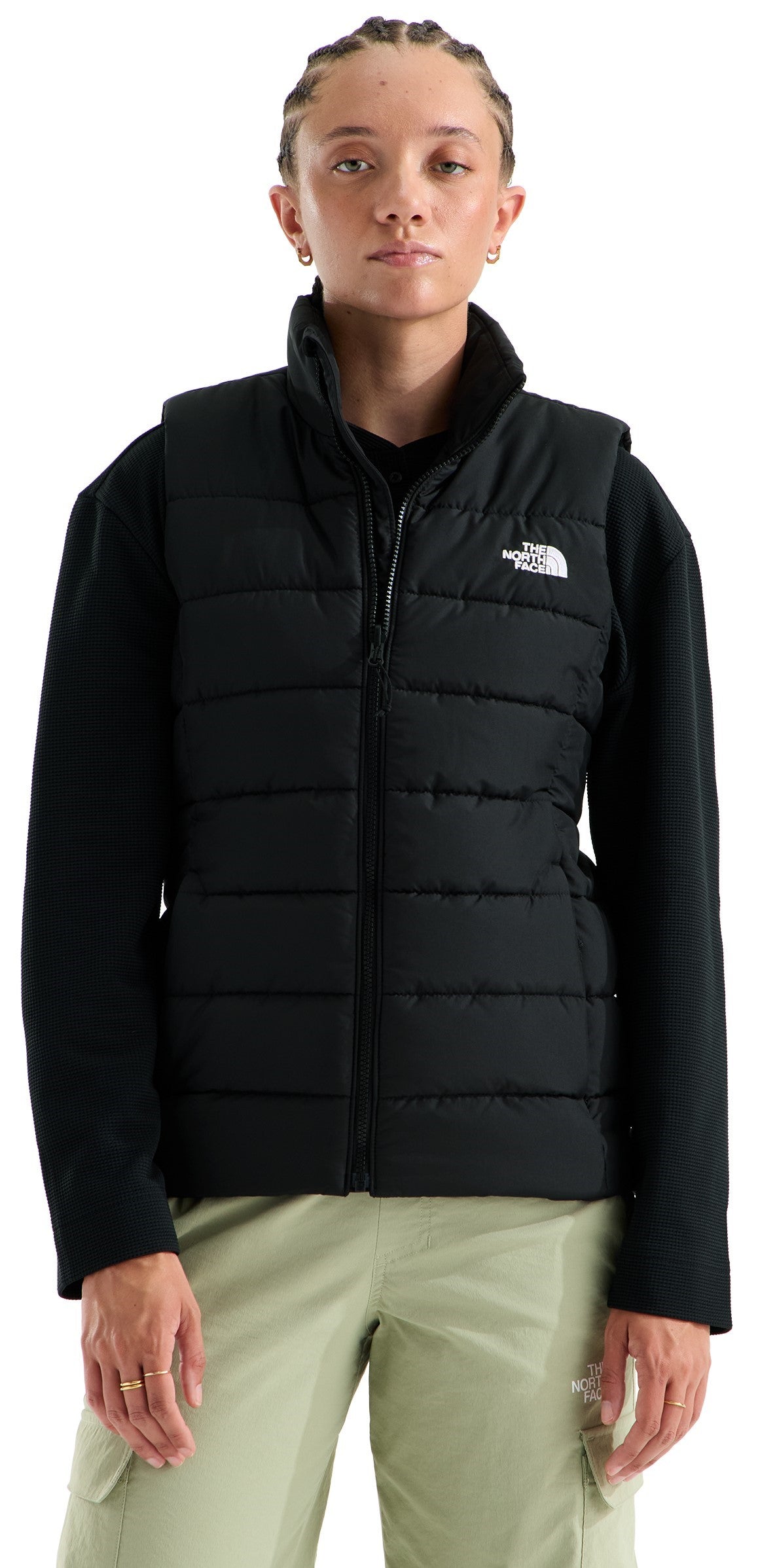 A person wearing a black quilted puffer vest over a black long-sleeved shirt and light sage green cargo pants with The North Face logo visible on the upper left chest.