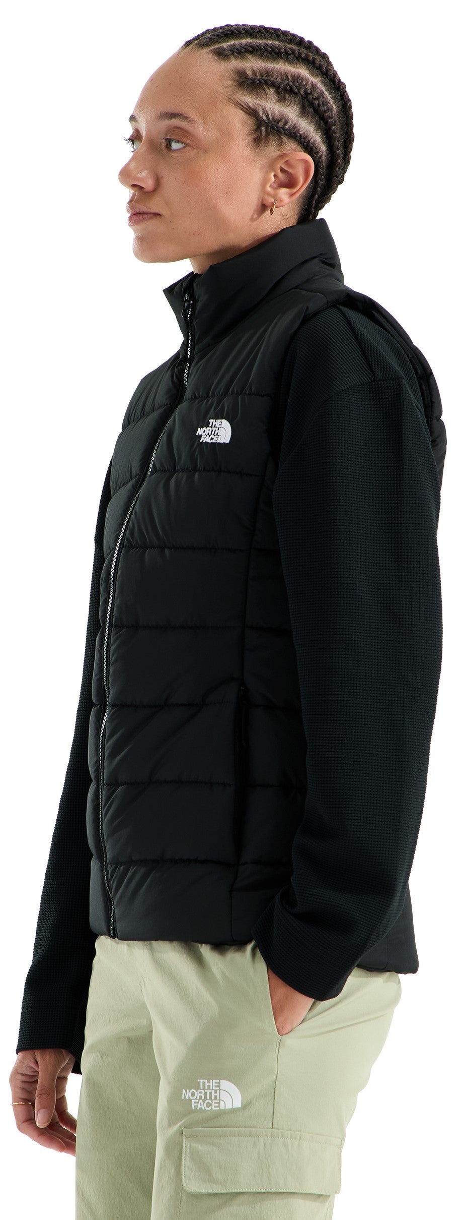 A person viewed from the side, wearing a black puffer vest over a black long-sleeved shirt with light green cargo pants, featuring the brand name The North Face on both the chest of the vest and the pocket of the pants.
