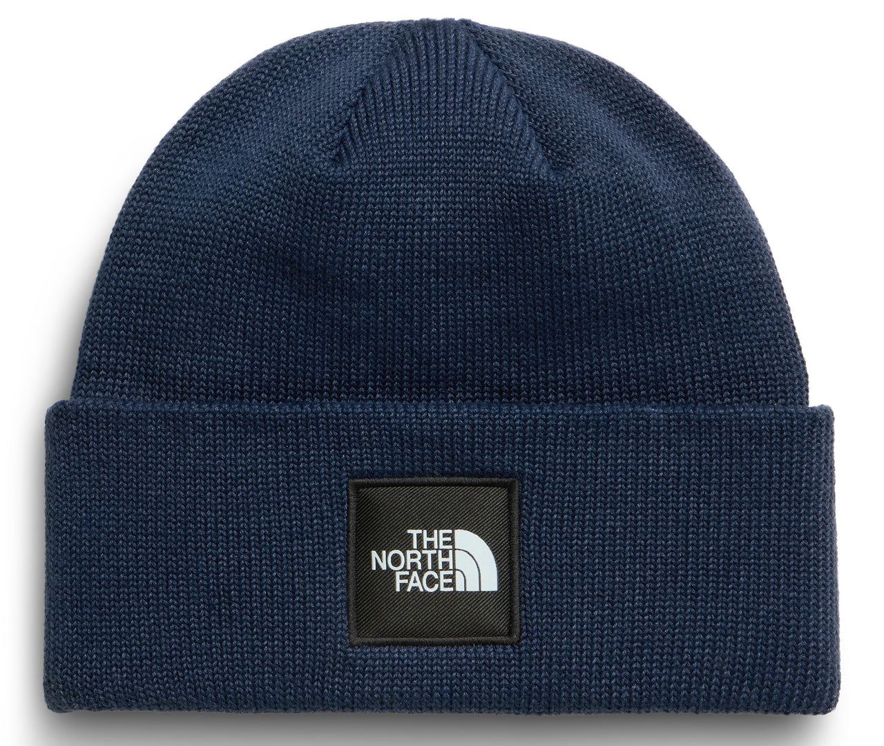 A dark blue ribbed knit beanie with a square black patch on the folded brim featuring white text that reads THE NORTH FACE.