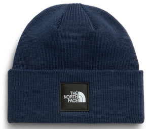 A dark blue ribbed knit beanie with a square black patch on the folded brim featuring white text that reads THE NORTH FACE.