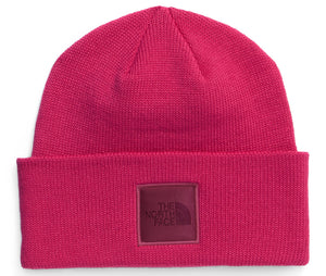 A bright fuchsia knit beanie with a folded cuff and a square patch on the front featuring the text THE NORTH FACE.