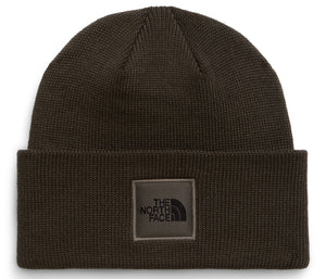 A dark olive green knit beanie with a folded cuff featuring a square patch on the front that displays the text THE NORTH FACE and a mountain silhouette logo.