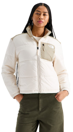 A woman wearing a cream and light tan color-blocked puffer jacket with a mock neck collar and a zippered chest pocket, paired with olive green pants.