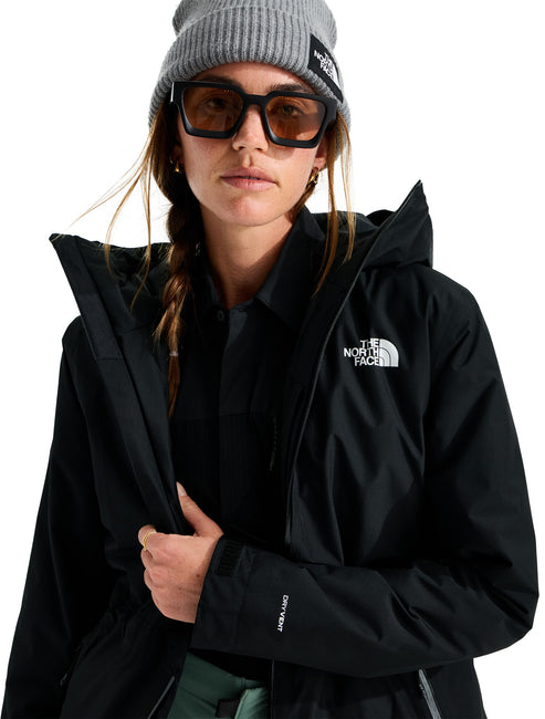 A person wearing a black, hooded, waterproof jacket with DryVent branding on the sleeve, a grey ribbed beanie with a small logo patch, and dark-framed sunglasses, posed against a white background.