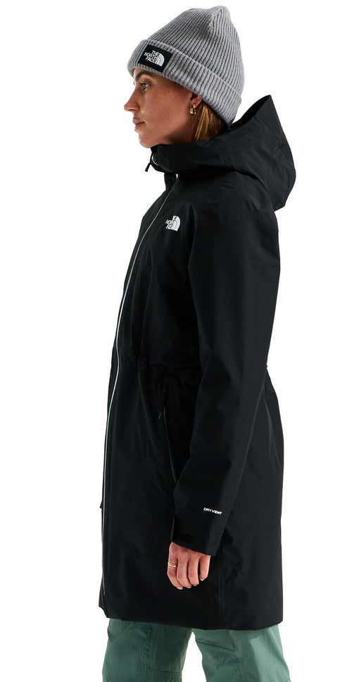 A woman seen from the side, wearing a black, hooded, knee-length rain jacket with a full-length zipper and a grey ribbed beanie hat.