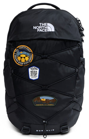 A black backpack with a bungee cord system on the front, adorned with three embroidered patches and the text THE NORTH FACE at the top and BOREALIS at the bottom.