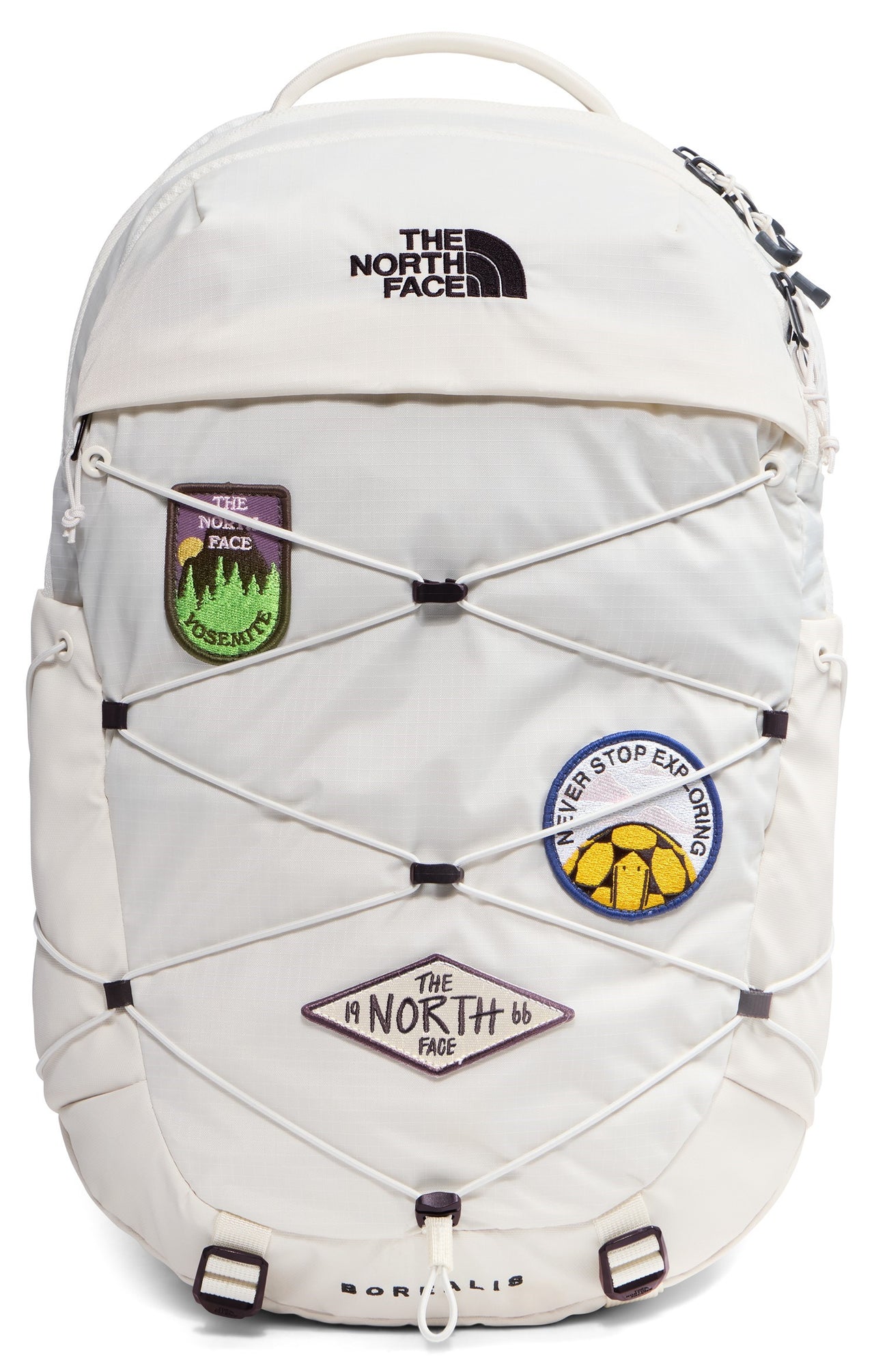 A white backpack with a bungee cord system on the front, featuring three patches: a Yosemite forest patch, a Never Stop Exploring patch, and a The North Face 1966 diamond-shaped patch, with the brand name printed at the top.