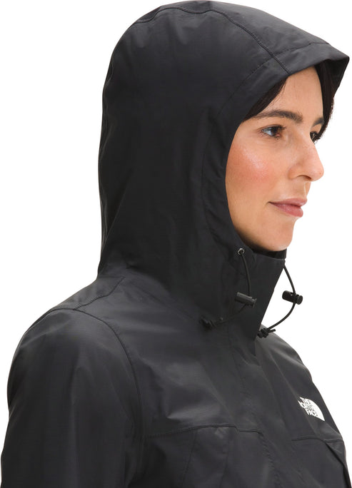 A woman shown in profile view wearing a black hooded rain jacket with an adjustable drawstring hood, featuring the logo visible on the upper chest.