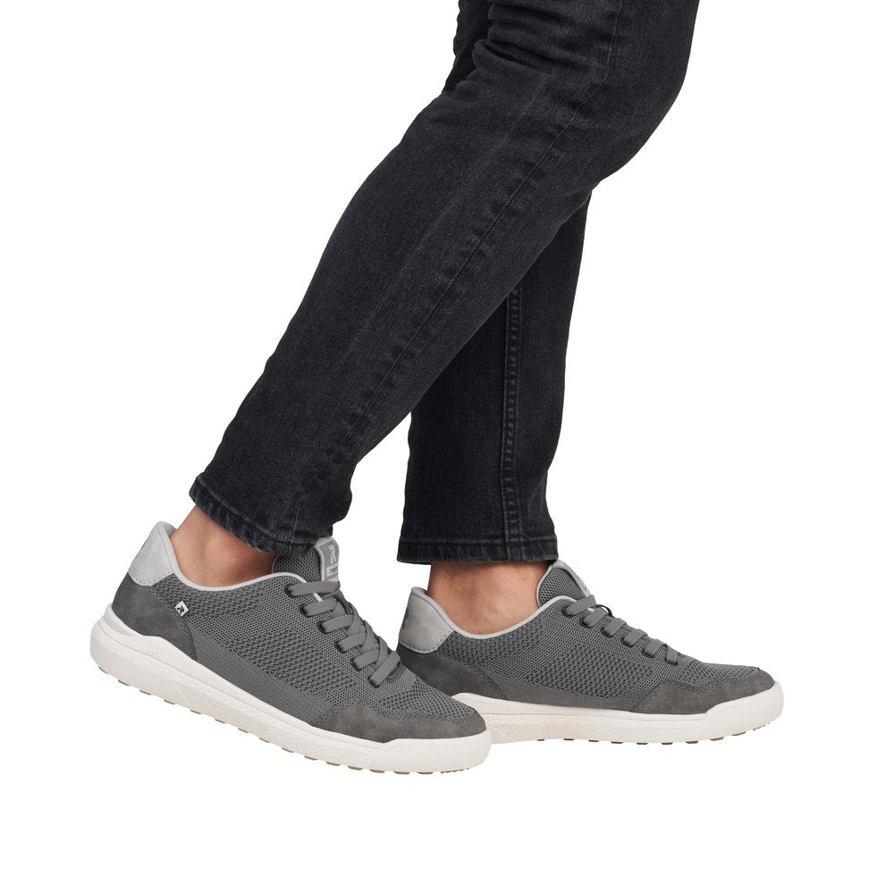 Person in jeans wearing gray tennis shoes with white soles.