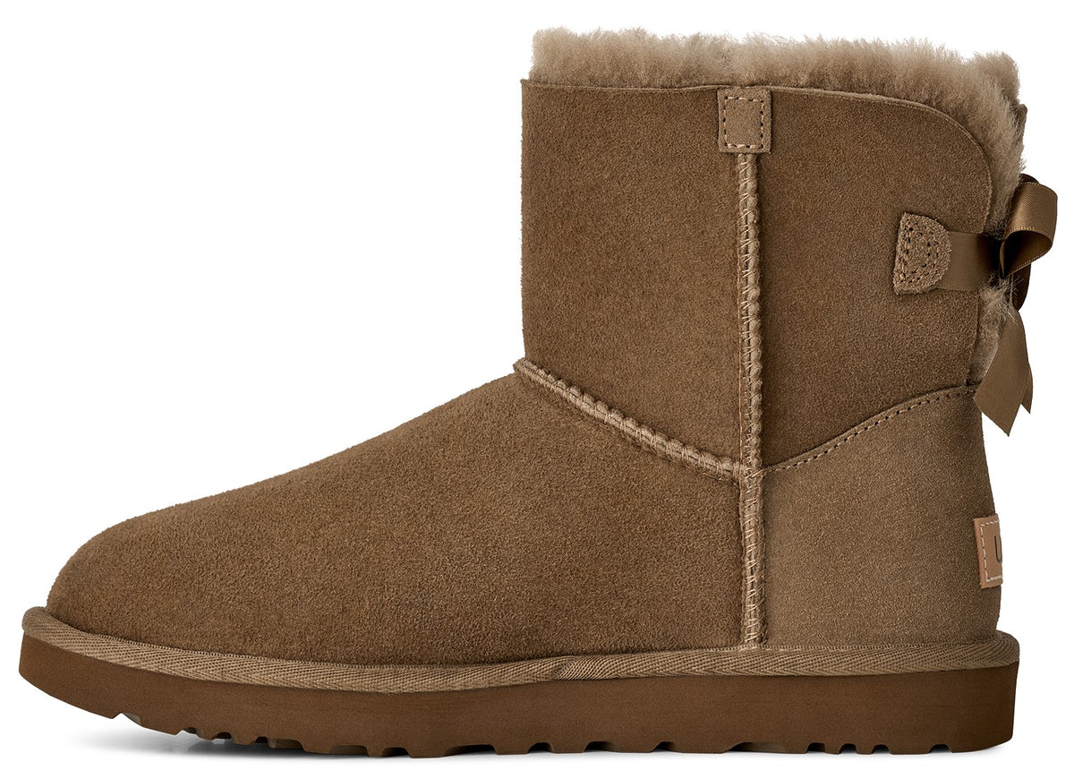 A tan suede boot with a round toe, thick rubber sole, sheepskin lining at the cuff, and a decorative bow on the heel.
