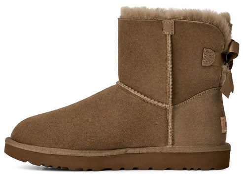 A tan suede boot with a round toe, thick rubber sole, sheepskin lining at the cuff, and a decorative bow on the heel.