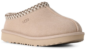 A tan suede slip-on slipper with a chunky platform sole and a decorative braided trim around the collar, featuring the embossed text UGG on the side.