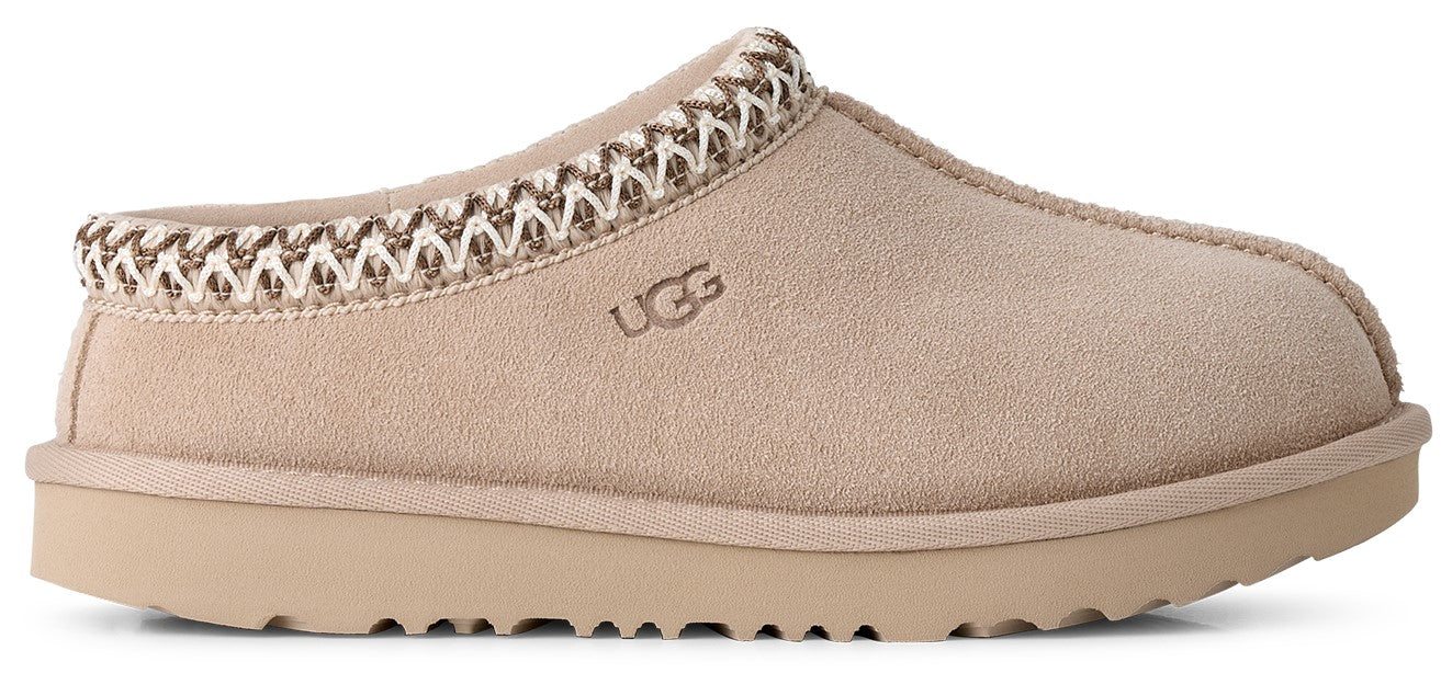 A light tan suede slip-on shoe with a thick rubber sole and a braided decorative trim around the collar, featuring the embossed text UGG on the side.