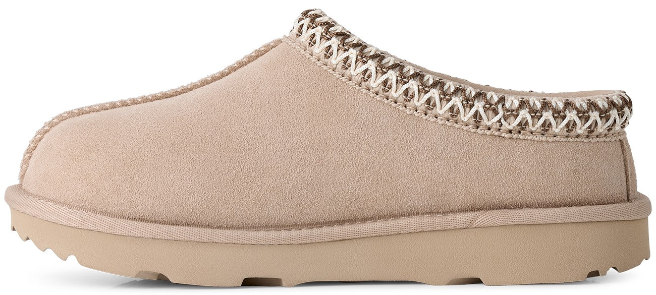 A beige suede slip-on mule slipper with a thick rubber sole and a decorative braided trim around the collar.