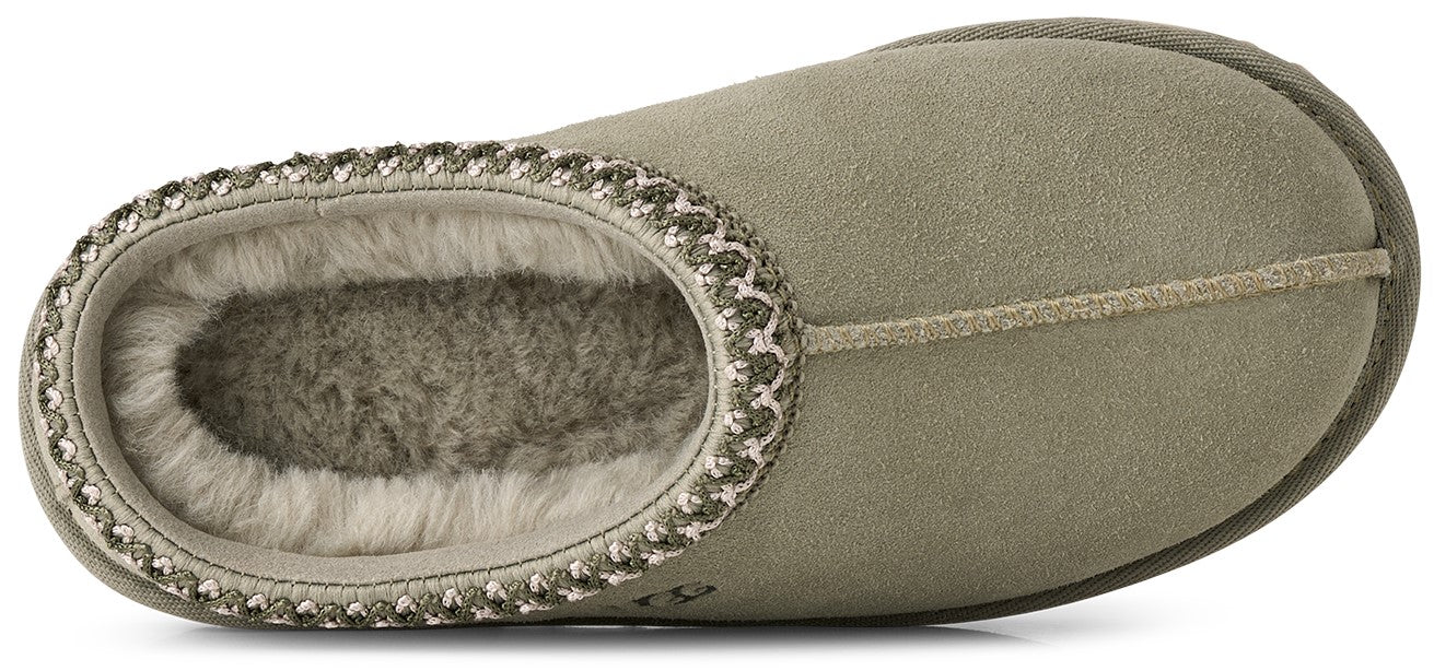 A top-down view of a light olive-green suede slipper featuring a soft, grey faux-fur lining and a decorative braided trim around the opening.