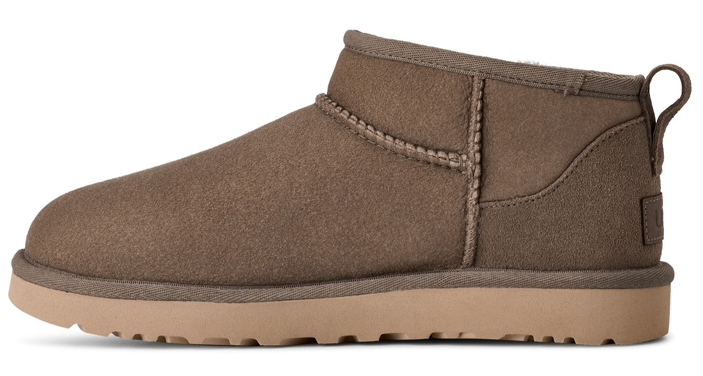 Side view of a short, taupe-colored suede boot with a tan sole and a loop on the back.