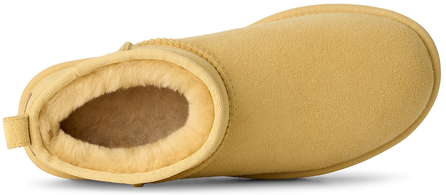 A top-down view of a mustard-yellow suede ankle boot with a fuzzy, beige shearling-lined interior.