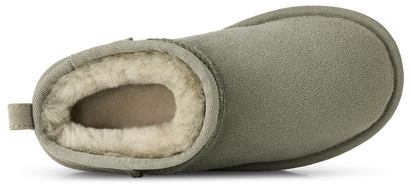 A top-down view of an olive green suede bootie lined with thick, cream-colored shearling, featuring a pull tab at the heel and a rounded toe.