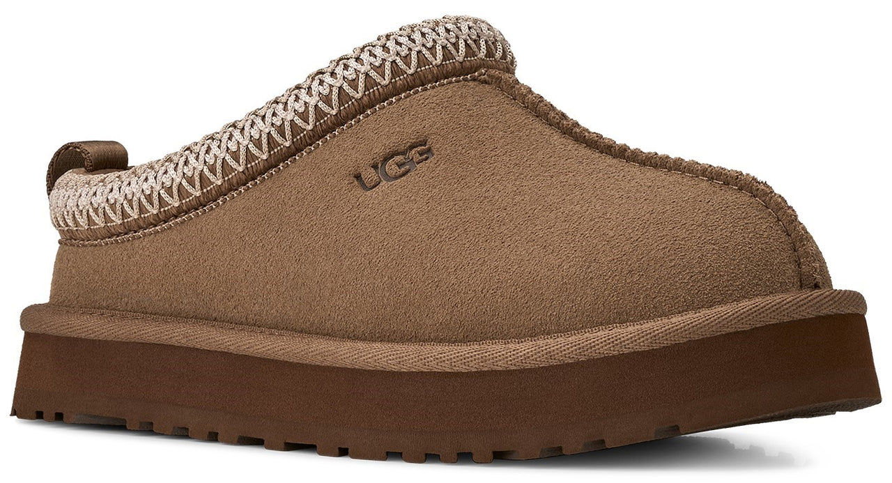 A tan suede platform slipper with a thick brown rubber sole, a woven beige and brown trim along the collar, and the logo UGG embossed on the side.