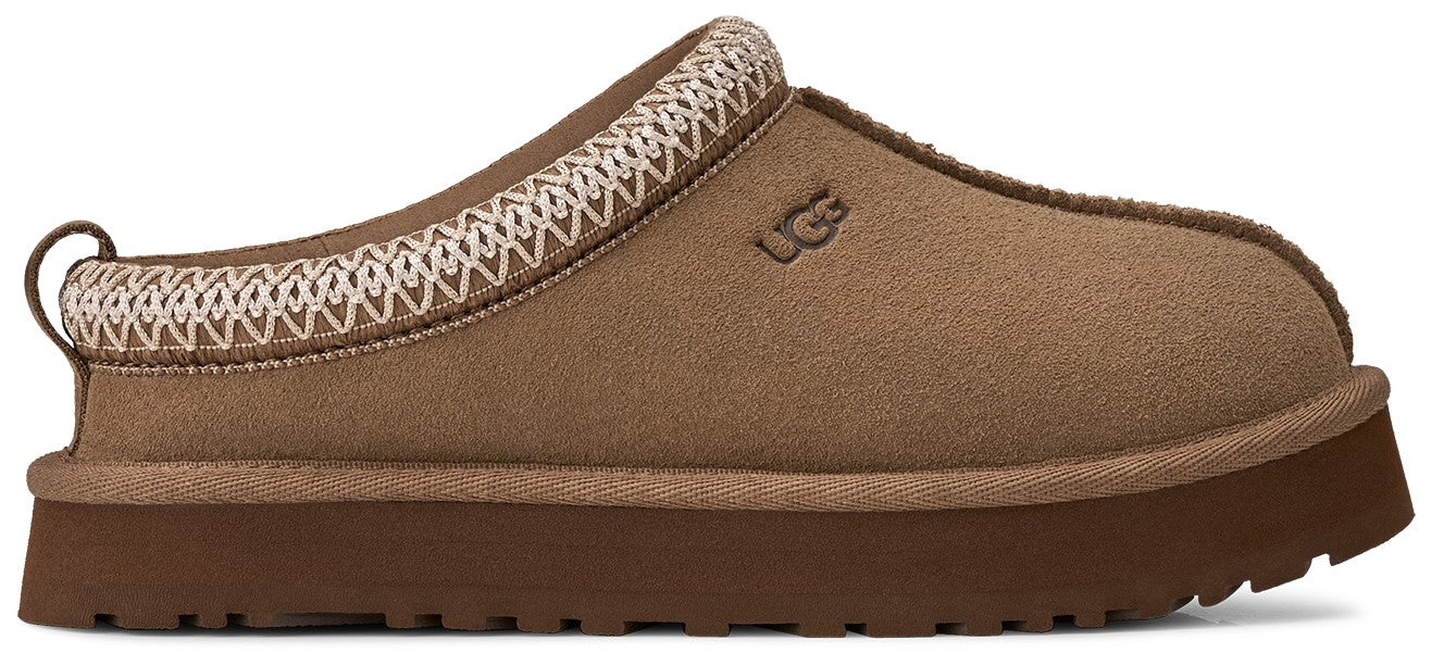 A brown UGG Tasman platform slipper featuring a thick dark brown sole, a soft suede upper with the brand logo embossed on the side, and a decorative braided trim around the collar.