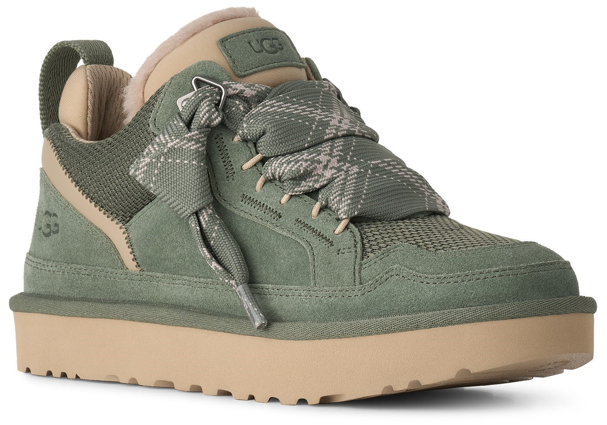 A low-top sneaker in sage green suede and mesh with a tan platform sole and thick, plaid-patterned laces.