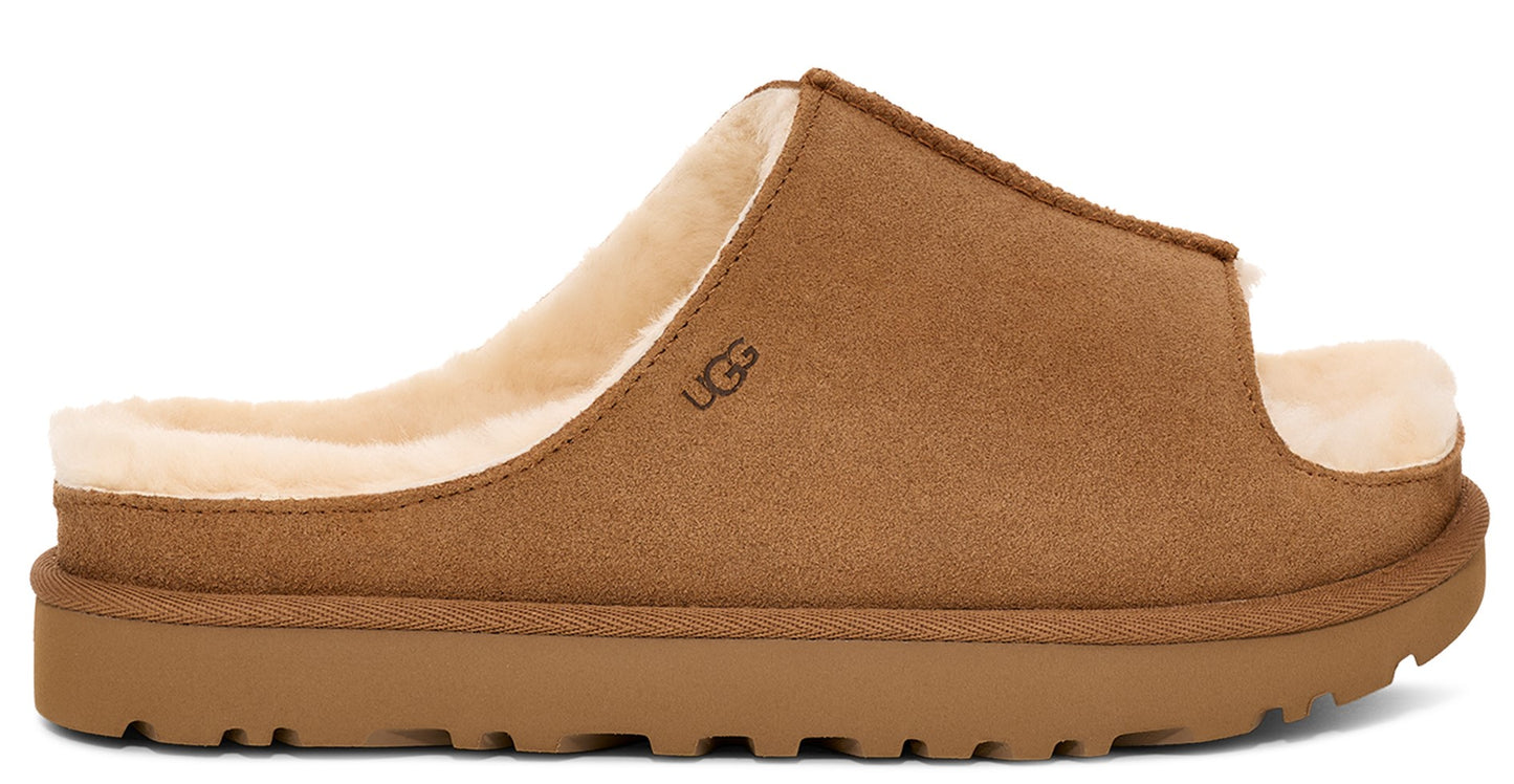 Side-view of a tan slide style slipper with shearling lining and logo.