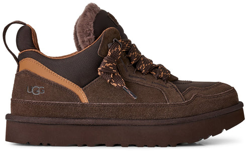 Side view of a dark brown suede sneaker with a thick rubber sole, fur trim around the ankle, patterned laces, and a small UGG logo on the side heel.