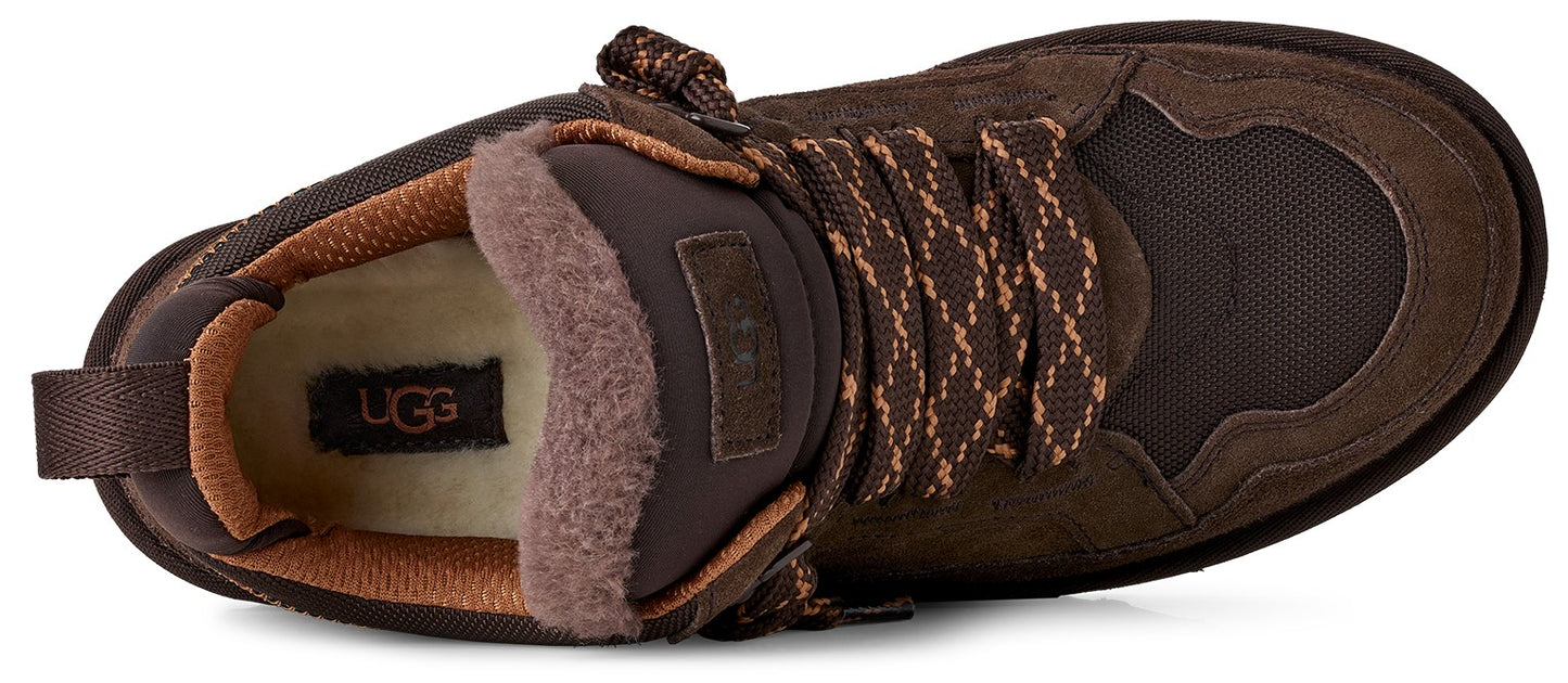 A top-down view of a dark brown suede and nylon winter boot with a cream-colored fleece-lined collar, featuring patterned brown laces and an UGG brand label on the insole.