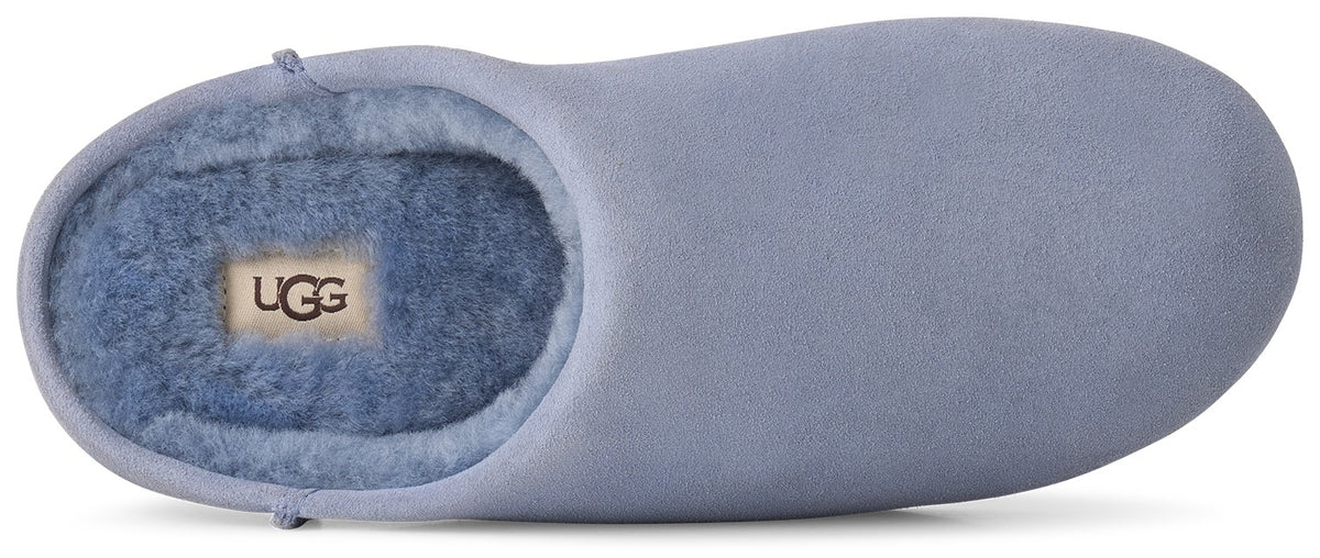 A light periwinkle blue suede slipper with a plush matching faux-fur interior lining and an UGG brand tag visible on the insole.