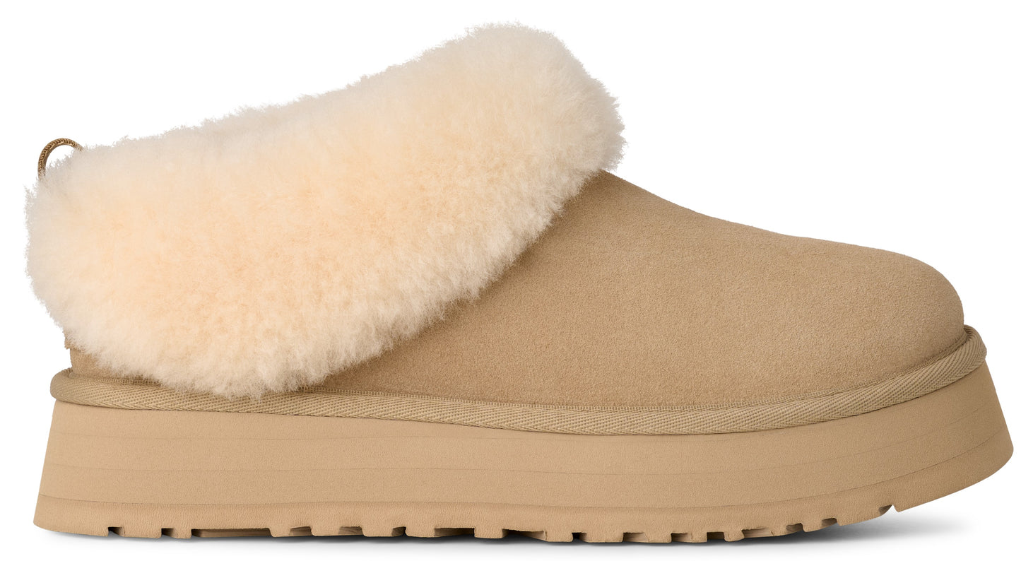 Tan suede slipper with a cream-colored shearling cuff and a thick sole.