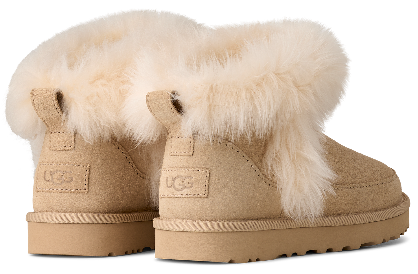 A pair of beige ankle boots with faux fur trim around the ankle and the logo 'UGG' on the heel.
