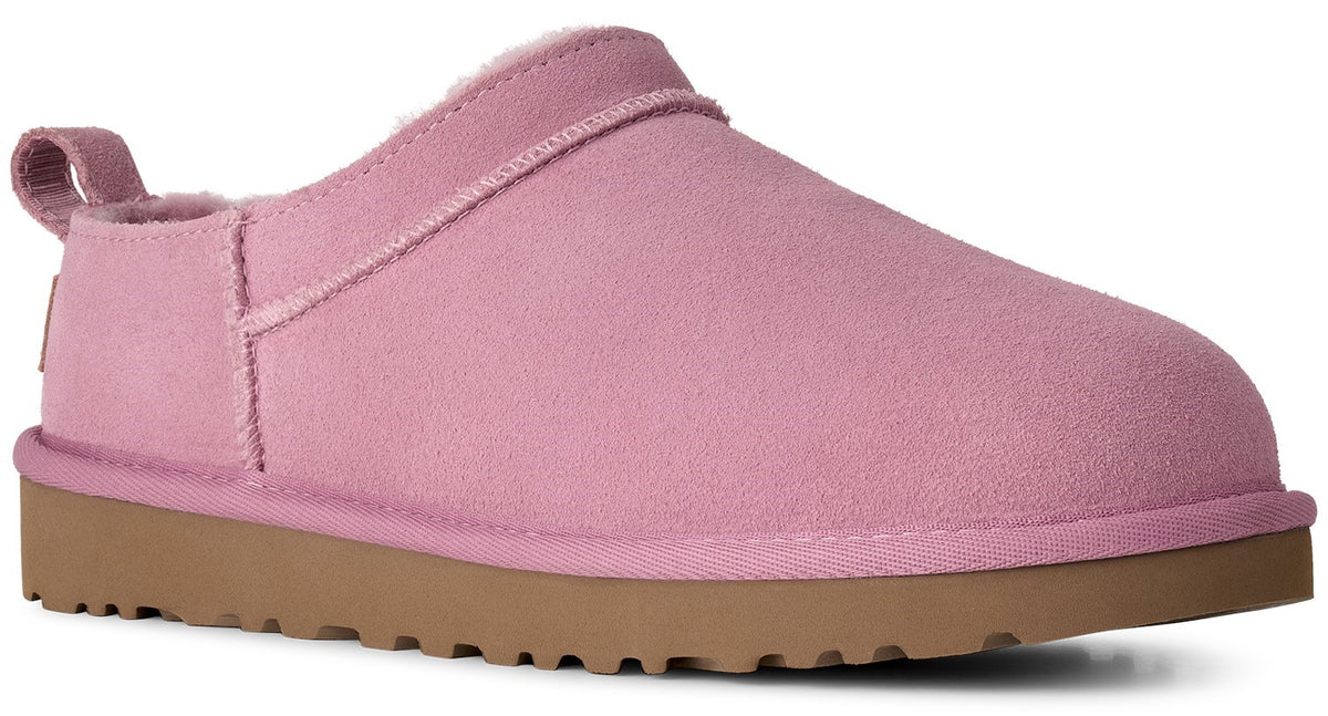 A light pink suede slipper with a brown rubber treaded sole, a low-profile slip-on design, and a small pull tab on the heel.