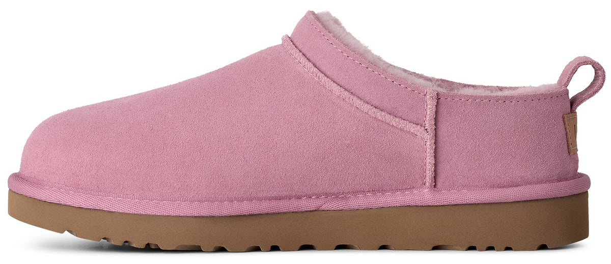 A pink suede slip-on shoe with a thick brown rubber sole, featuring a fur-lined interior and a small pull tab at the heel.