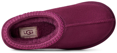 A top-down view of a dark magenta suede slipper featuring a soft, fuzzy interior lining and a decorative braided trim around the opening, with an UGG label visible inside.