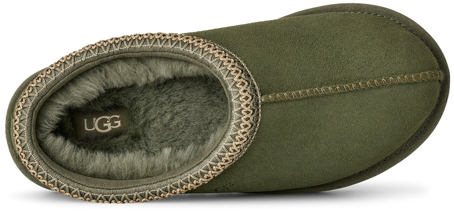 A top-down view of an olive green slipper lined with soft, matching green faux fur, featuring a decorative braided fabric trim around the collar and a visible UGG logo label on the insole.