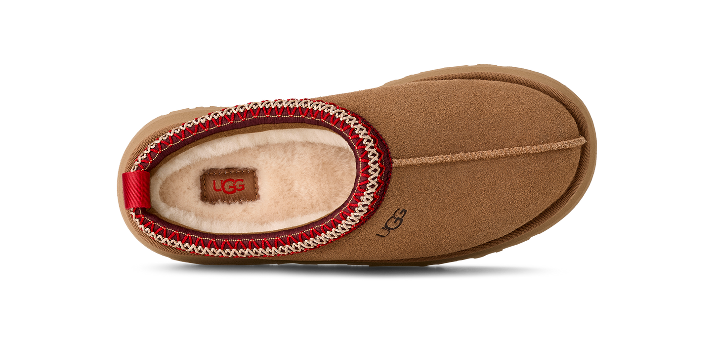 Tan UGG slipper with red and white trim.