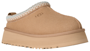 Tan slip-on shoe with a thick platform sole and a white-trimmed opening, with the brand logo visible.