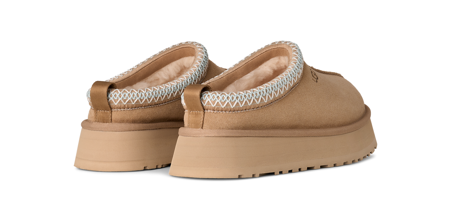 A pair of backless, tan shoes with white trim around the ankles and flat, ridged soles.
