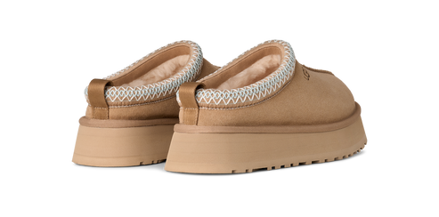 A pair of backless, tan shoes with white trim around the ankles and flat, ridged soles.