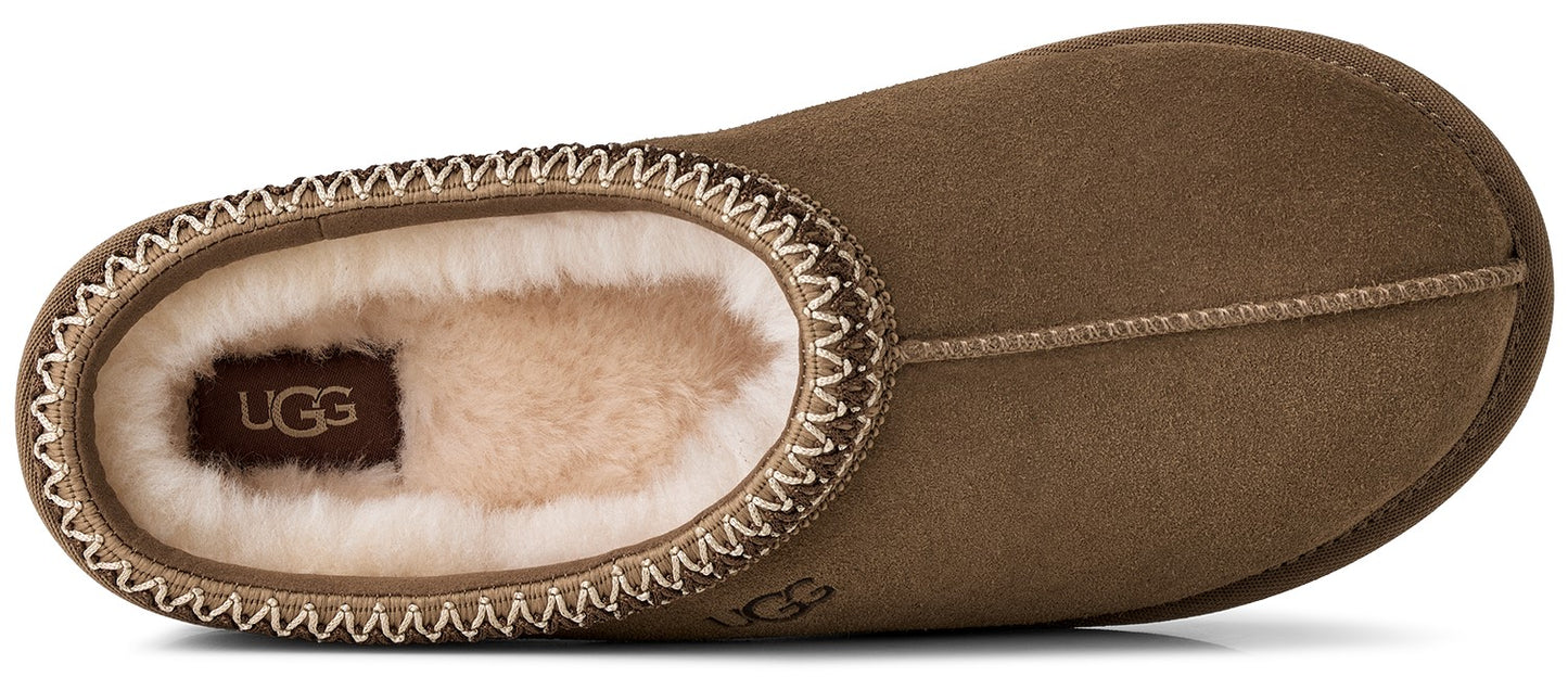 An olive green suede slipper with a cream-colored shearling lining, a decorative stitched trim around the collar, and the label text UGG visible on the insole and the side of the heel.