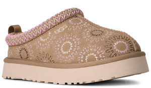 Mule style shoe with tan suede printed with sunburst patterns in tan and pink and pink braided trim at the top of the shoe and a tan rubber sole.