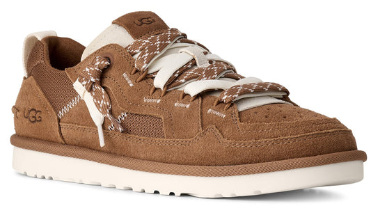 A brown suede sneaker with a white sole, featuring thick white and brown patterned laces, a tan tongue and heel, and a small logo on the side.