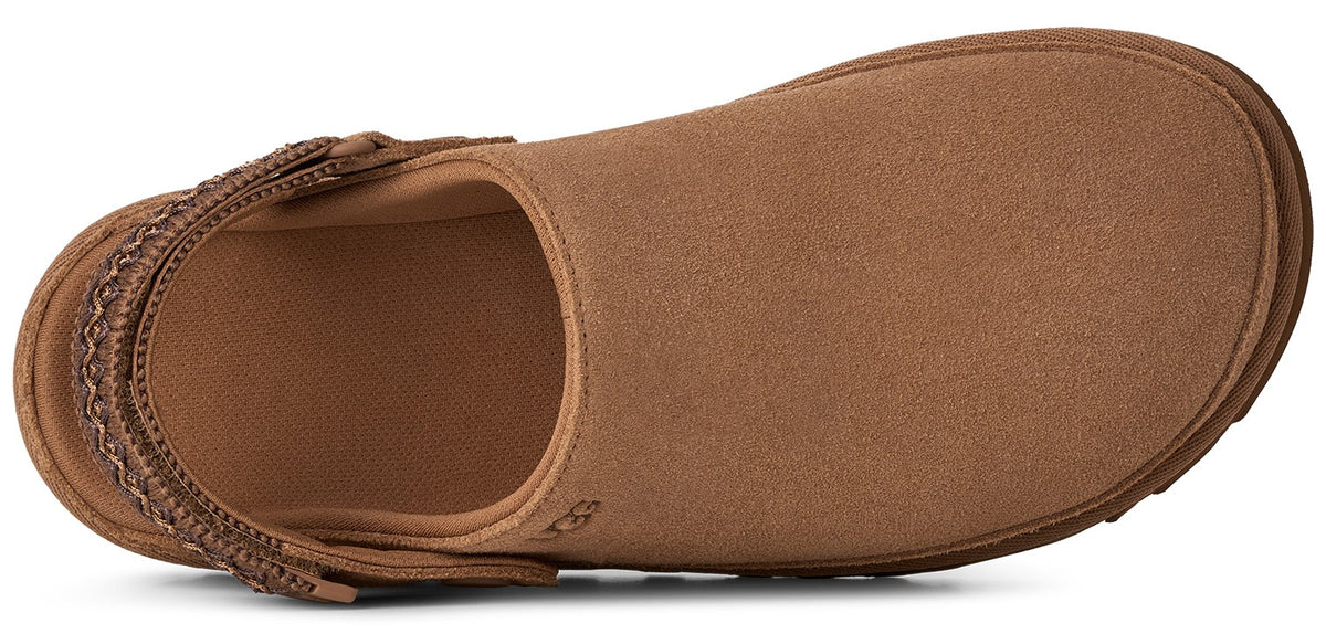 A top-down view of a tan suede slip-on shoe with a rounded toe and an adjustable woven strap across the heel.