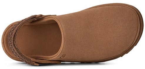 A top-down view of a tan suede slip-on shoe with a rounded toe and an adjustable woven strap across the heel.