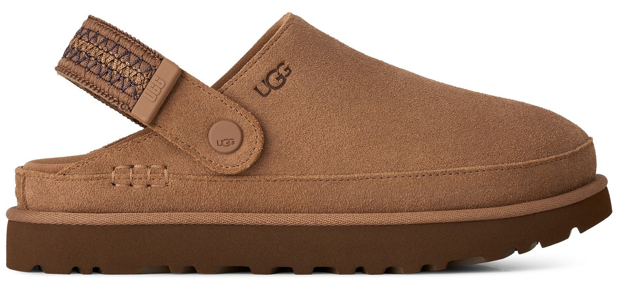 A tan suede slip-on shoe with a dark brown sole and a decorative woven strap around the heel, featuring a small UGG logo embossed on the side.