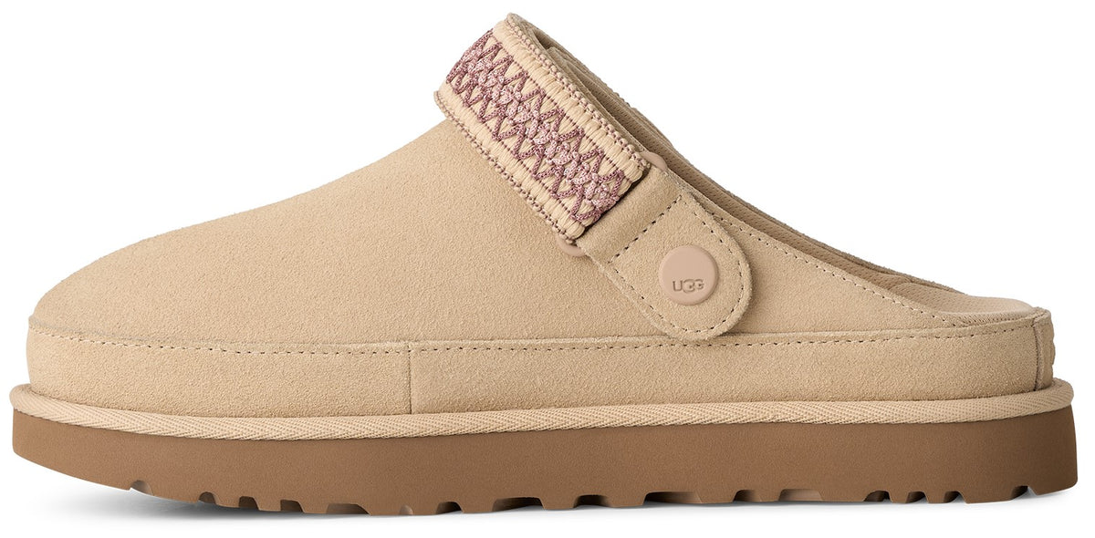 A light tan suede slip-on shoe with a thick brown rubber platform sole, featuring an adjustable woven strap across the top with a small circular logo button on the side.