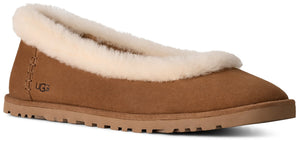 A tan suede slipper with a rounded toe, a flat rubber sole, and a white plush shearling trim along the collar, featuring the brand name UGG embossed on the heel.