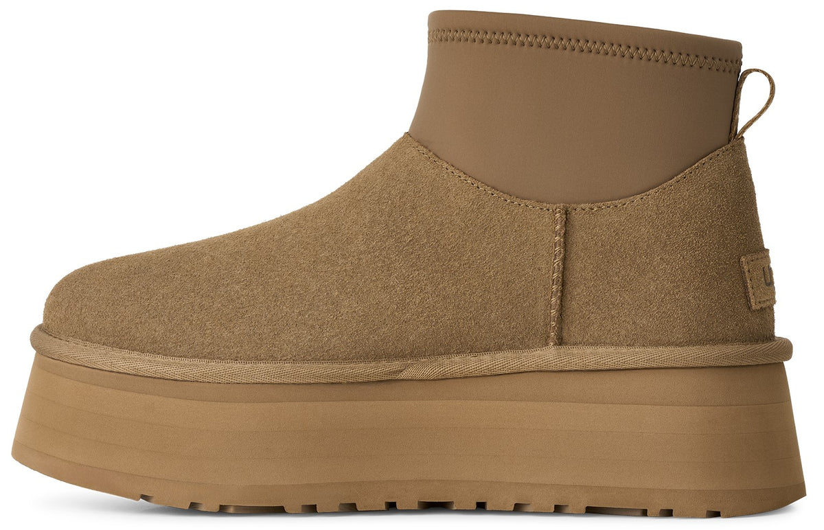 A tan-colored platform boot with a suede upper, a higher ankle cuff made of a smoother material, and a thick, chunky rubber platform sole.