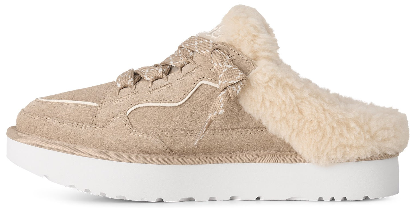 A beige suede slip-on sneaker with a thick white platform sole and a fluffy cream-colored shearling lining that spills over the collar, featuring beige patterned laces on the front.